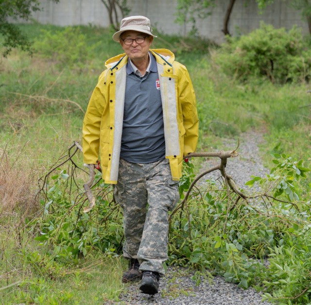 Environmental Engineer Dr. Kim Chom Tong cheerfully drags two trimmed branches along the walking path of the Camp Carroll Wetland during a spring cleanup event, Republic of Korea, April 29, 2022. The Camp Carroll Wetland is an environmental reclamation project located near Camp Carroll&#39;s main gate. It provides a number of biological and hydrological benefits, including water filtration.