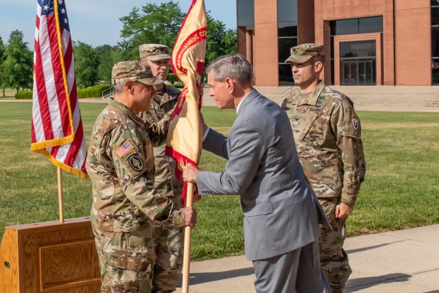 Col. Anthony Pollio, incoming U.S. Army Garrison Fort Leonard Wood commander (left), accepts the U.S. Army Installation Management Command guidon from Vince Grewatz, director of U.S. Army Installation Management Command – Training at Joint Base Langley-Eustis, Virginia, as Col. Jeff Paine, outgoing garrison commander (right) looks on during a change-of-command ceremony today on the Maneuver Support Center of Excellence Plaza. 