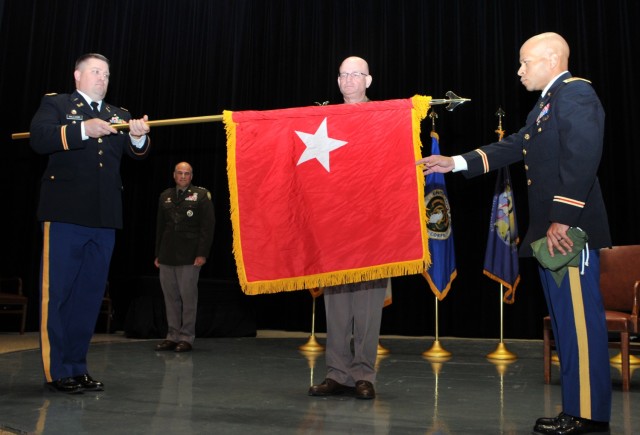 Brig. Gen. Samuel L. “Luke” Peterson looks on as Maj. Zane Williams (left) and Maj. Jude Coe unfurl his one-star flag.  Lt. Gen. David G. Bassett, director, Defense Contract Management Agency, promoted Peterson from colonel to brigadier general during the June 30 ceremony. 