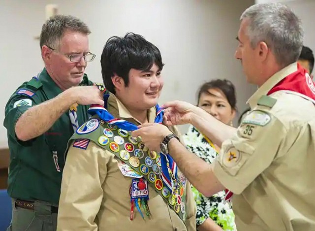 Kim McCann, left, who now serves as the physical security manager at Kure Pier 6 in Japan, places an eagle scout neckerchief on his son, Ian, during a ceremony in 2014. McCann said he still volunteers as a Boy Scout leader in honor of his son, who unexpectedly died shortly after becoming an eagle scout. 