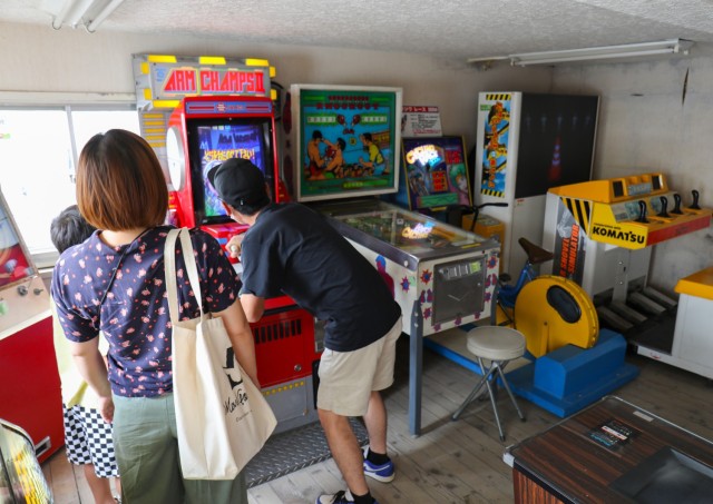 A family plays a classic arcade game while in a waiting room for the Used Tire Market in Sagamihara, Japan, July 22, 2022. Located about a 10-minute drive from Camp Zama, the shop has arcade games as well as more than 100 retro vending machines, many of them from the 1970s and 80s, that offer a variety of food items. People can also just come by and admire the machines without buying anything.