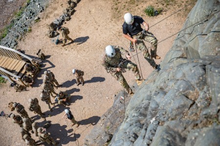 Mountaineering instructors from Northern Warfare Training Center Staff Sgts. Jordan Weeg, right, and Garrett Phillips, left, rappel down a rock face while 11th Airborne Division Soldiers watch from below during Advanced Military Mountaineering Course 8 July at Black Rapids Training Site.