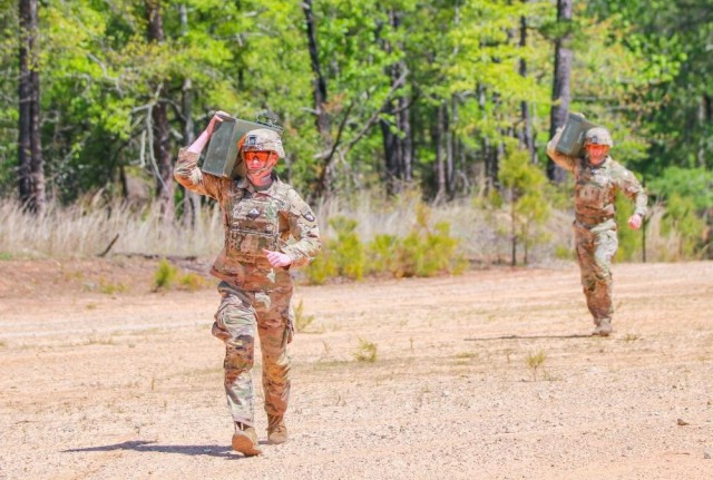 U.S. Army Soldiers carry ammunition cans while wearing body armor.