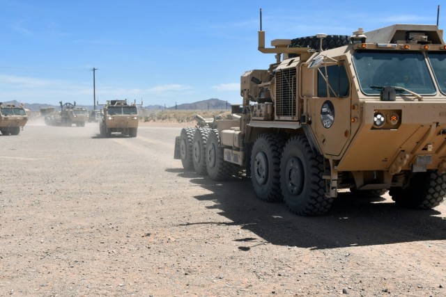 A convoy of semi-autonomous palletized load system vehicles roll past attendees during a vehicle dedication ceremony April 10, 2019,  at Fort Bliss, Texas, for 16 fallen Soldiers from the motor operator transport military occupational specialty.