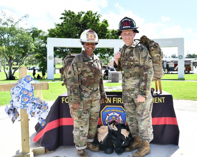 Fort Buchanan Garrison Commander Col. Tomika M. Seaberry wears the Fort Buchanan Assistant Fire Chief helmet and Garrison Command Sgt. Maj. Roderick W. Hendricks wears the Fort Buchanan 9/11 helmet as they stand by the wooden cross stand holding...