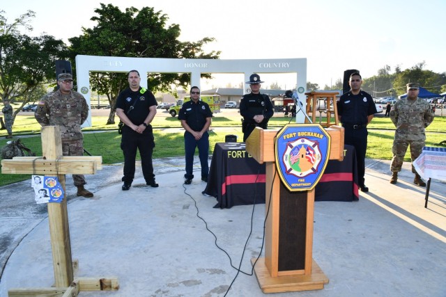 Representatives of Soldiers, Emergency Medical Service/First Responders, Firefighters, Police, Firefighters, Army Religious Support Soldier pose behind the display in commemoration of 9/11. On the left is the wooden cross built by Fort Buchanan...