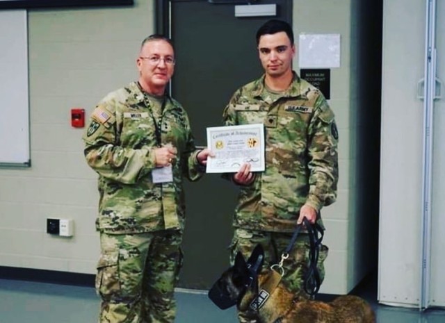 Maj. Gen. Miller presents Spec. Justin Ane, (Patrol Explosive Detector Dog), 2D MP DET (MWD) Fort Meade, MD,  with a certificate of achievement and the Provost Marshal General’s coin of excellence for his great handling skills which helped locate a missing person.