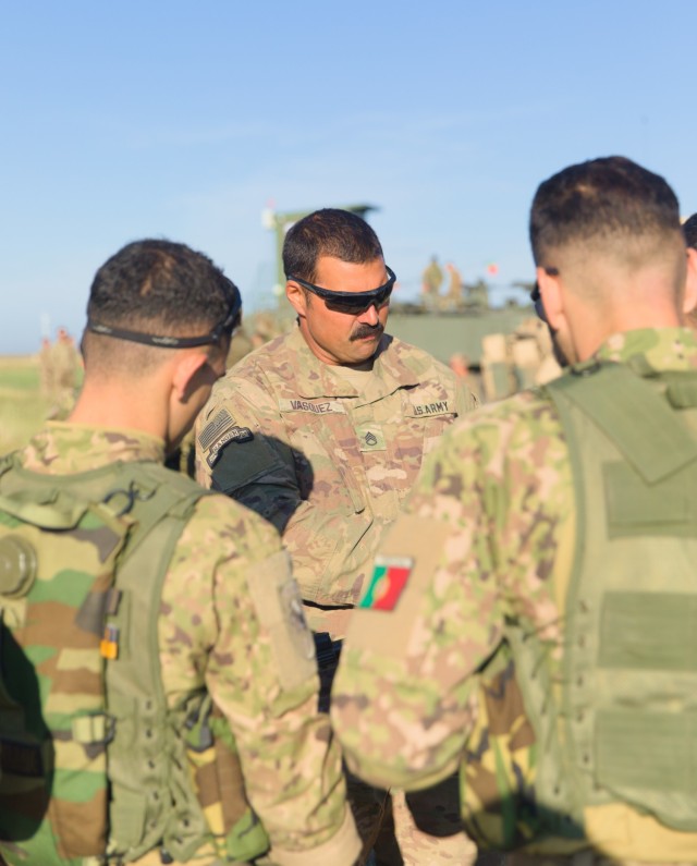 U.S. Army Staff Sgt. Kristofer Vasquez, an infantryman assigned to Alpha Company, 1st Battalion, 8th Infantry Regiment, 3rd Armored Brigade Combat Team, 4th Infantry Division, briefs Portuguese soldiers on U.S. weapon systems during Exercise Justice Eagle, at Smardan Training Area, Romania, on Sept. 17, 2022. Under command and control of the 101st Airborne Division (Air Assault), 1st Battalion, 8th Infantry Regiment continues to reinforce NATO’s eastern flank and engage in multinational exercises like Justice Eagle with Allies and partners across the European continent to reassure our Nation’s Allies.  