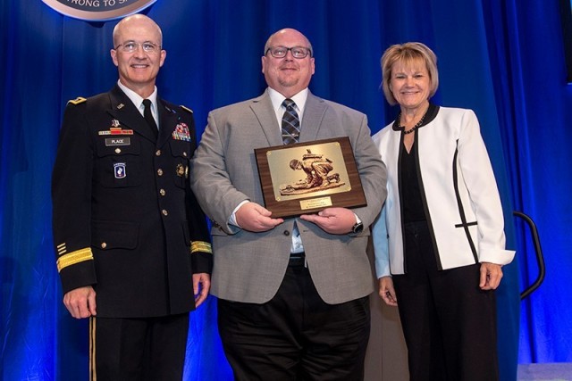 Frederick Brozoski (center) receives the Distinguished Service Award at the 2022 Military Health System Research Symposium presented by Ms. Seileen Mullen (right), Acting Assistant Secretary of Defense for Health Affairs. Also pictured is Lt. Gen. Robert J. Place (left), Director of the Defense Health Agency.