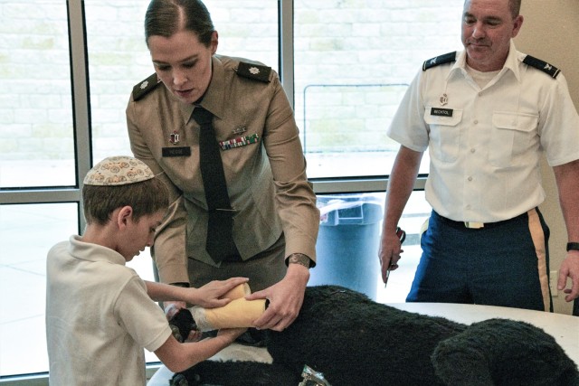 Lt. Col. Sara Hegge, center, and Col. Dewey Bechtol, right, demonstrate how to dress a notional wound on the Diesel Canine Simulator to a student at the Torah Academy of San Antonio, during the school’s Veterans Day Program, November 11, 2022.  Hegge and Bechtol, both veterinarians assigned to the U.S. Army Medical Center of Excellence (MEDCoE) spent their Veterans Day sharing their unique stories of service with the students. The Veterinary Corps is responsible for animal medicine, public health, food protection, and research.  During the one-hour hands-on presentation, the students, ranging from kindergarten to 7th grade also got to experience what it is like to have a job in the Army Veterinary Corps like examining kosher Army Meals-Ready-to-Eat using methods similar to the Corps’ food inspectors and even got to meet a military working dog in-training named “EEphy”. 