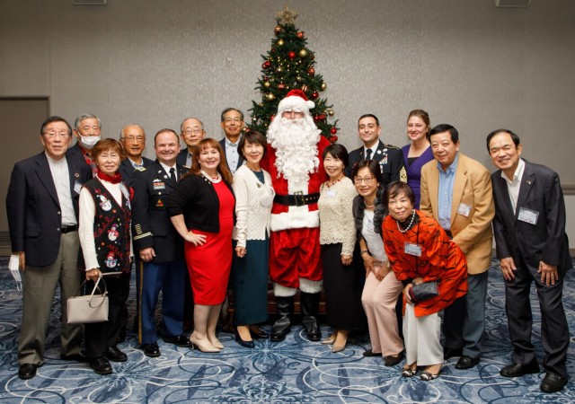 Col. Christopher L. Tomlinson, commander of U.S. Army Garrison Japan, and Command Sgt. Maj. David A. Rio pose for a photograph with guests during a holiday reception at the Camp Zama Community Club, Japan, Dec. 9, 2022. 