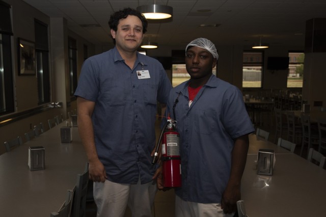 Anthony Vasquez (left) and Zamario Cooper, Fort Leonard Wood Bldg. 908 dining facility employees, pose with one of the DFAC’s fire extinguishers on Monday. The two have been roommates in a home in St. Robert for four years, and used fire extinguisher training they received at work to save their home and possessions when a grease fire started on Dec. 4 in their kitchen. 