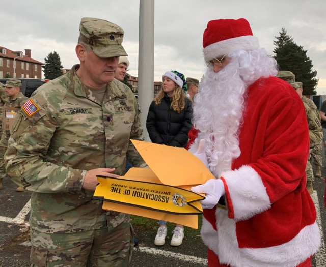 Lt. Col. David DeHart receives an envelope of gift cards from Santa Claus to be distributed to selected junior enlisted service members with families on JBLM.
