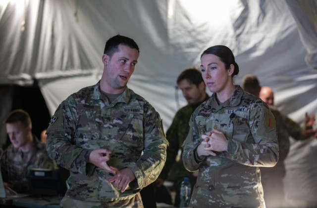 U.S. Army Staff Sgt. Austin Morse, left, an intelligence  noncommissioned officer in charge assigned to the 1st Infantry Division (1 ID) and U.S. Army Maj. Jessica Kitchell, an intelligence operations officer with the 1 ID, converse during Winter Strike 22, a command post exercise held in Bolesławiec, Poland, Dec. 12, 2022. The 1 ID is working alongside NATO allies and regional security partners to provide combat-credible forces to V Corps, America’s forward deployed corps in Europe.