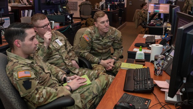 Pennsylvania National Guard Joint Operations Center operations noncommissioned officers Sgt. John Marru, Staff Sgt. James R. Ergott, and Sgt. Christopher R. Galbraith participate in a winter storm tabletop exercise from the JOC floor Dec. 20, 2022, at Fort Indiantown Gap, Pa. The exercise designed to improve and validate domestic response procedures. (This photo has been altered to obscure an ID card.)