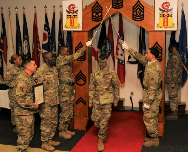 Sgt. Baylee Hopper, center, walks under a wooden arch adorned with all the noncommissioned officer ranks and a pair of raised sabers to be officially inducted into the NCO corps during a ceremony at Sagami General Depot, Japan, Jan. 11, 2023. 