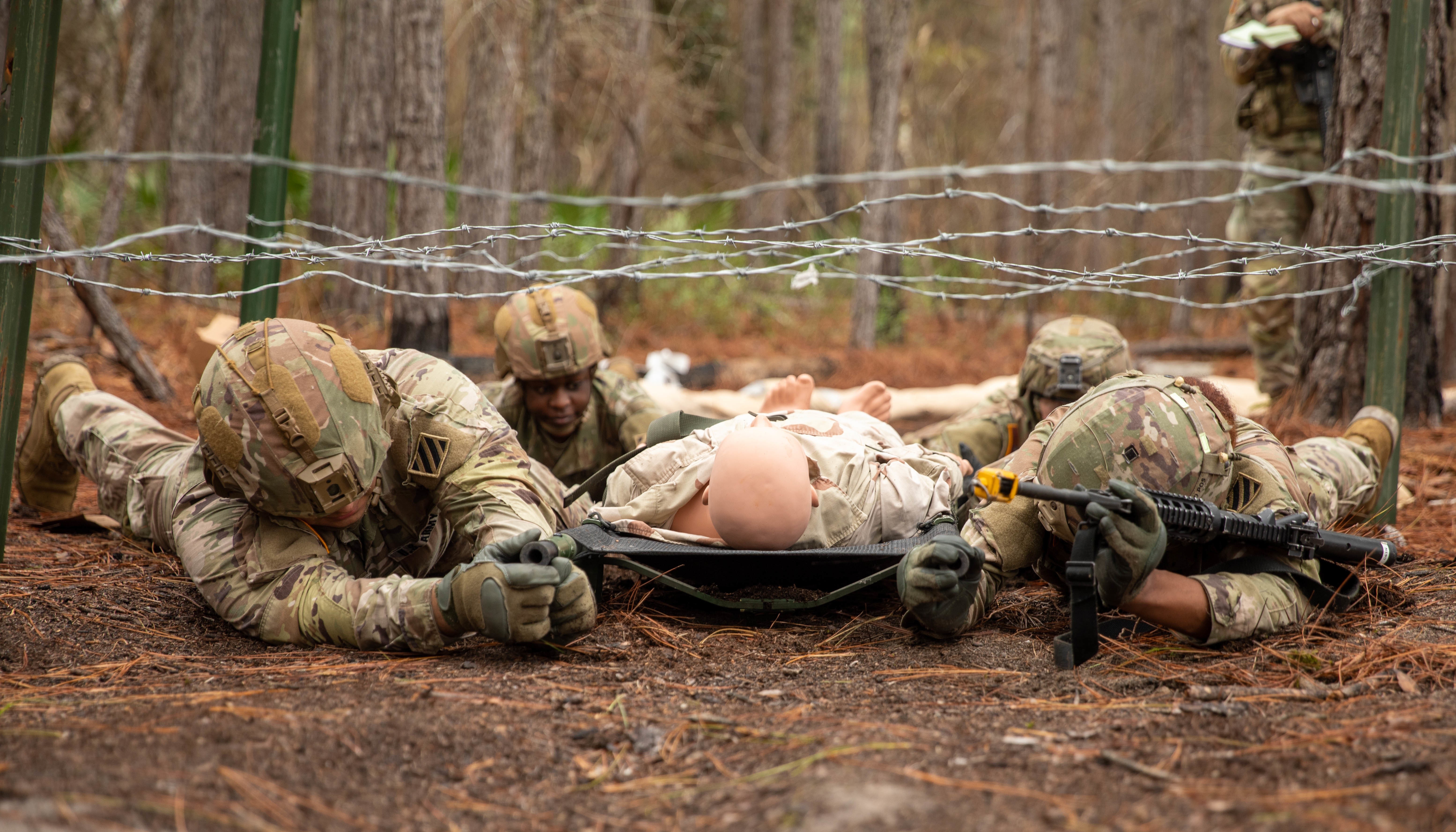 Soldiers from the 3rd Infantry Division low crawl with a simulated casualty for the Expert Field Medical Badge on Fort Stewart, Georgia, Jan. 18, 2023. In order to earn the badge candidates must complete a written test, a physical fitness assessment, day and nighttime land navigation courses, various warrior skills, tactical combat casualty care, evacuation lanes, a 12-mile foot march and disassemble, reassemble and function check their M4 riles; validating themselves as Army medical professionals and distinguishing themselves amongst their peers. 
