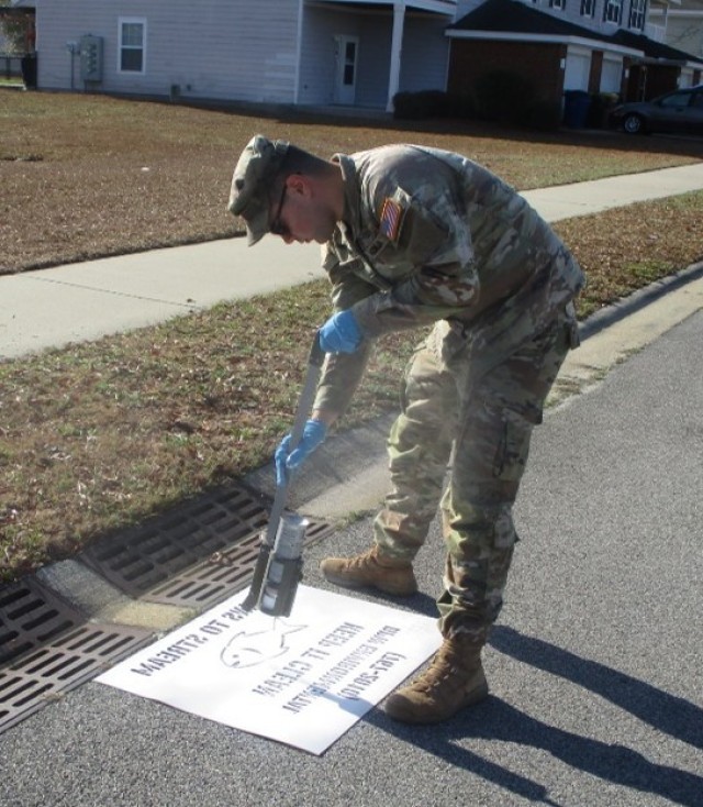 Pfc. Pedro Almeida, 14th Field Hospital, paints a message on a stormwater drain in the Liberty Woods housing area, Feb. 7 on Fort Stewart.