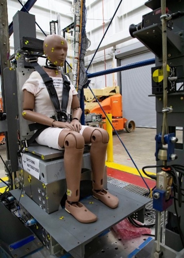 Caption: A close-up of an instrumented female test dummy in a rigid seat prepared for a test run on the USAARL vertical acceleration tower.


