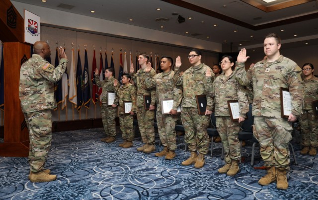 Nearly 20 noncommissioned officers recite an oath as they are inducted into the NCO corps during a ceremony at the Camp Zama Community Club, Japan, March 22, 2023.