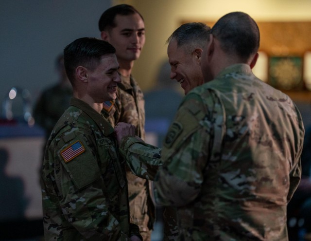 Spc. Dimitry Boylan, left, a Paratrooper assigned to Delta Company, 2-504 Parachute Infantry Regiment, receives the Army Commendation Medal from Major Gen. Christopher LaNeve, commander of the 82nd Airborne Division, after winning the first ever 82nd Airborne Division Innovation Drop Zone Competition on Fort Bragg, N.C., March 29, 2023. Boylan, alongside 1st Lieutenant Christopher Bruce, also of Delta Company, 2-504 PIR, presented a concept for a flip-down keypad display unit, a remote-control system essential to the radios in use by paratroopers across the Division. 