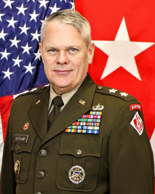 Maj. Gen. Richard Heitkamp wearing a uniform poses in front of the American flag on the left, and a two-star general officer flag on the right