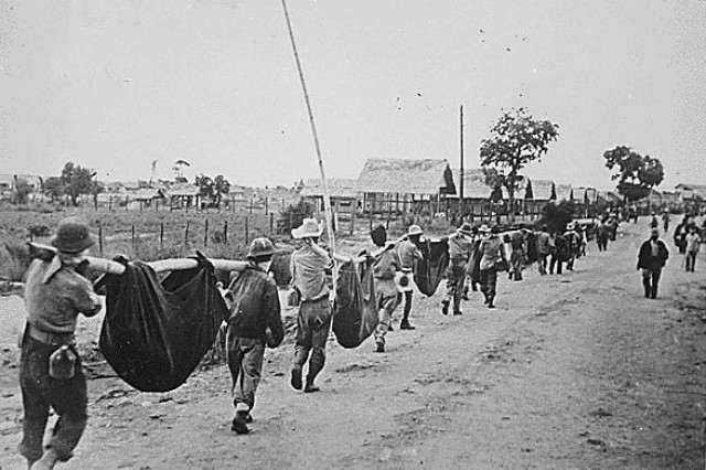 A photo by the Japanese depicts American prisoners in the Philippines using improvised litters to carry their comrades who, from the lack of food or water during the Bataan Death March, fell along the road in May 1942.