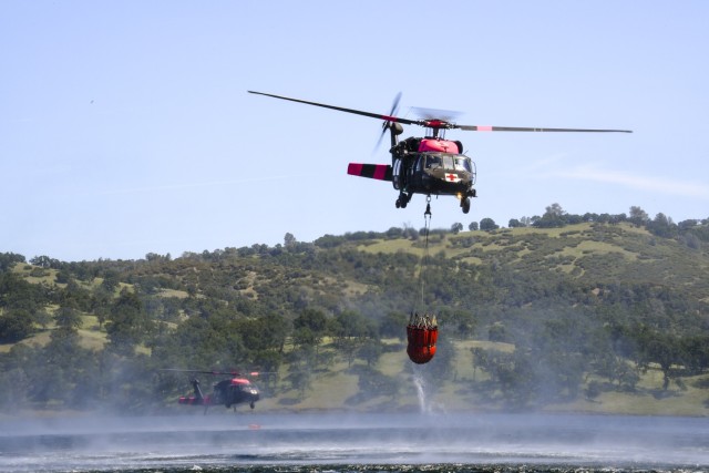 Two U.S. Army UH-60 Black Hawk medium utility helicopter from the 1-140th Aviation Regiment dips their water bucket bucket in the Pardee Reservoir during annual joint aerial fire fighting training near Ione California, April 27, 2019. California Army and Air National Guard helicopters units train together alongside Cal Fire. The partnership enhances California aerial wild land fire fighting capabilities. (U.S. Air National Guard photo by Staff Sgt. Christian Jadot)