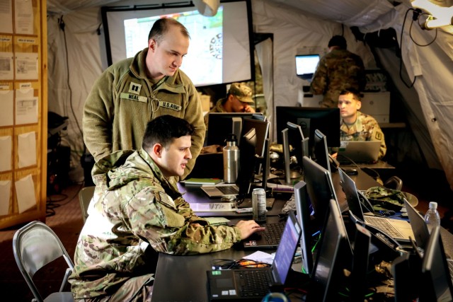 U.S. Army Capt. Craig Neal, a chemical, biological, radiological and nuclear officer at 30th Medical Brigade (top), helps Capt. Julio Rodriguez, a health services plans, operations, intelligence, security and training officer at 30th Medical Brigade (bottom) on his computer while trying to find documentation for a mission during a Command Post Exercise on Rhine Ordnance Barracks, Kaiserslautern, Germany on March 16, 2023. The Command Post Exercise was held to prepare junior Soldiers and senior leaders for Defender ‘23 using real world scenarios.