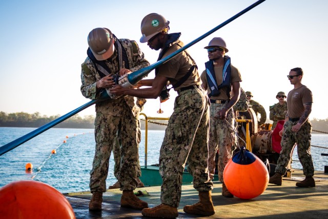 Navy Seaman Qwante Huggins, right, and Navy Petty Officer 3rd Class Joshua Banks, both assigned to Amphibious Construction Battalion 1, work to affix the buoy connector aboard the commercial Australian vessel Bandicoot during Exercise Talisman Sabre 23 in Weipa, Australia, July 21, 2023.