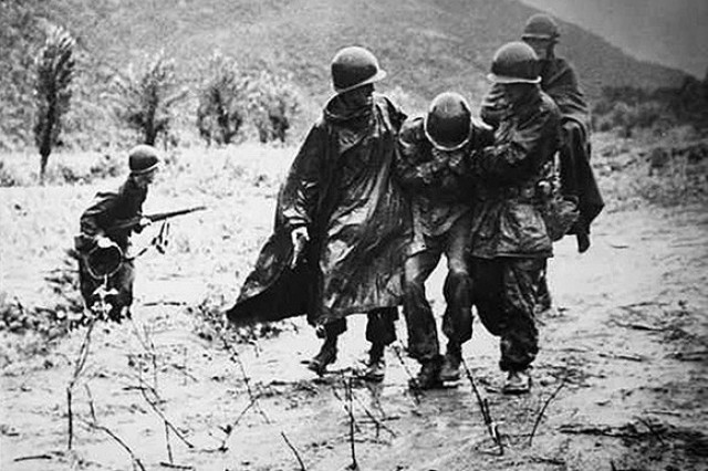 Army Chaplain (Capt.) Emil Kapaun (right) and Army Capt. Jerome A. Dolan, 1st Cavalry Division, carry an exhausted soldier off the battlefield in Korea, early in the war.