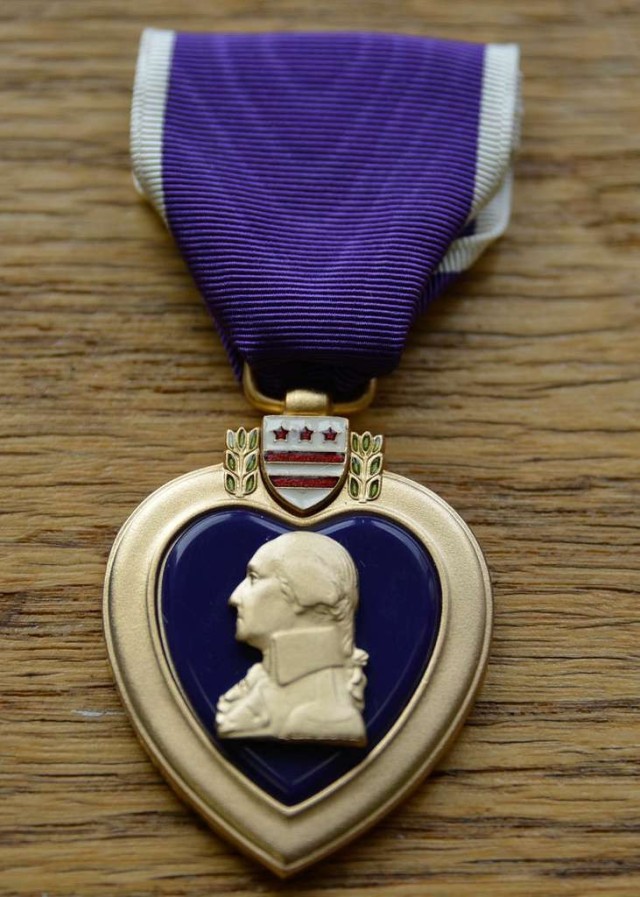 The Purple Heart medal lays flat on a wooden surface.