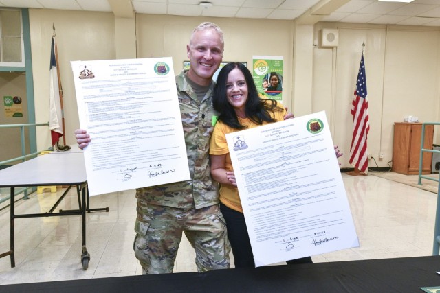 Lt. Col. Seam Riley, commander of the 187th Medical Battalion and Jennifer Emerson, Briscoe Elementary School Principal hold up copies of their Adopt-A-School program charter. The leaders signed the charter prior to the battalion donating school supplies to 315 students and families on Aug. 11, 2023.