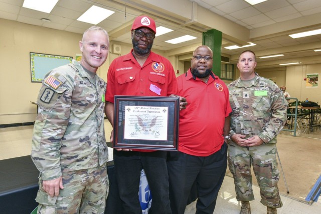 187th Medical Battalion Command Team Lt. Col. Sean Riley and Command Sgt. Maj. Jeremy Conn present a certificate of appreciation to members of the Royal Arch Masons Clifford Massey and Darrin Prute for their donation of backpacks to the students of Briscoe Elementary School. Members of the Royal Arch Masons joined the battalion in donating much needed school supplies to the students and families of Briscoe Elementary School on Aug. 11, 2023.