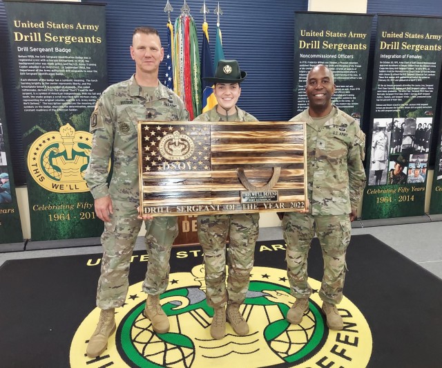Three military personnel with center one holding wooden plaque resembling the American flag.