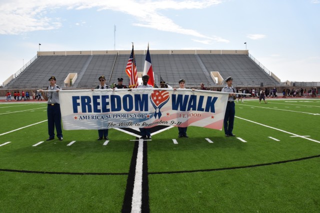 Cadets from the Killeen High School JROTC program pose with the Freedom Walk banner as attendees walk the track in the background at Leo Buckley Stadium during the Freedom Walk Monday at Killeen High School. (U.S. Army photo by Janecze Wright, Fort Cavazos Public Affairs)