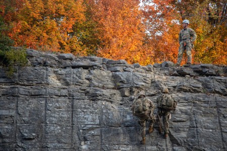 Soldiers from the 1st Brigade Combat Team, 10th Mountain Division ascend a cliff while carrying rucksacks during the alpine skills competition event on Fort Drum, New York, Oct. 5, 2023. The competition was the culminating event for Soldiers to use their mountaineering and cold weather survival skills they learned during Alpine Readiness Week.