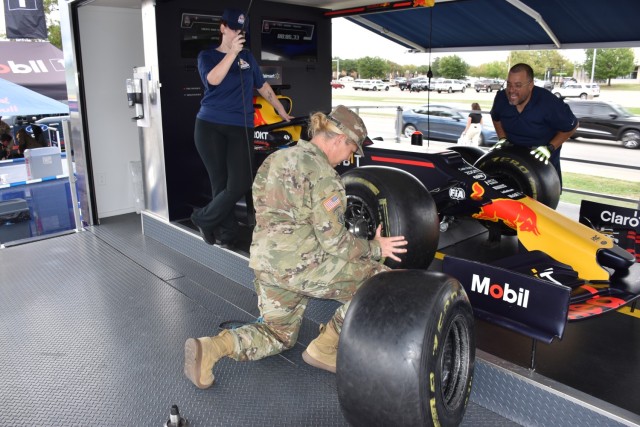 Adrian Nunez, Red Bull Pit Stop Tour manager, and Lucy Herdman, Red Bull ambassador, look on as Sgt. 1st Class Aleta Berry, Fort Cavazos Installation Reception Center, competes in the Red Bull Pit Stop Challenge Oct. 11 in the parking lot of the III Corps Express Shoppette. (U.S. Army photo by Janecze Wright, Fort Cavazos Public Affairs)