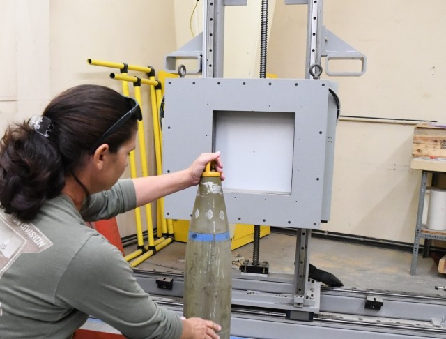 Radiography Technician Lindsey Carter holds a 155- round on the TXR panel for digital radiography. The machine can perform a nose and base x-ray. The team usually takes a 0- and 90-degree x-ray of each round.