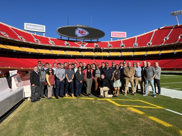 Information Operations Qualification Course students take a group photo with Kansas City Chiefs Vice President of Content and Production Rob Alberino, Jr., (front right) on GEHA Field at Arrowhead Stadium, Kansas City, Mo., Oct. 20, 2023.