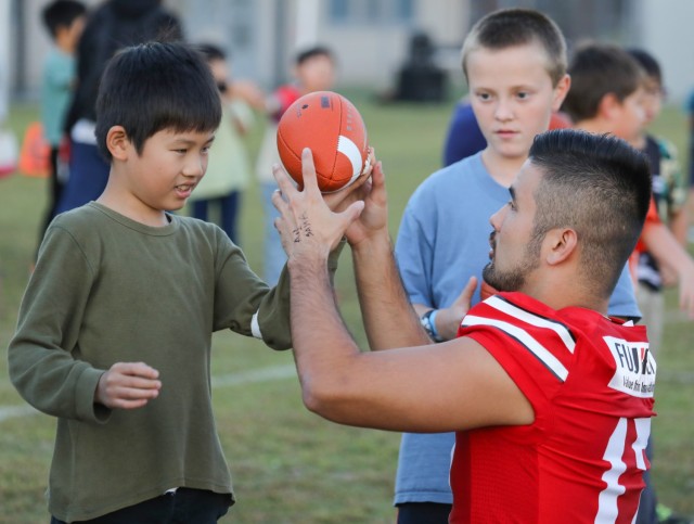 Ryuji Van Deusen, right, a professional football player for Ebina Minerva, shows children how to properly grip a football during a youth sports clinic at Sagamihara Family Housing Area, Japan, Nov. 3, 2023. The clinic, which had about 150 American and Japanese children attend, was the first event jointly hosted by U.S. Army Garrison Japan and Zama Junior Chamber International. 