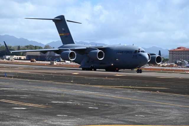 A C-17 flexes its wings as it taxis on the tarmac at Wheeler Army Airfield, its engines a low hum against the backdrop of a busy military hub.