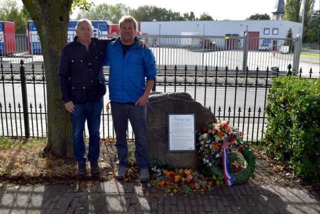 Two gentlemen stand next to a memorial. 