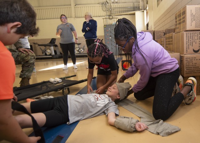 Wood Elementary School fifth graders wrap one of their fellow fitness club members in bandages and perform mock life-saving procedures, including a litter carry, Saturday morning at Shea Gym with the assistance of drill sergeants and cadre from...