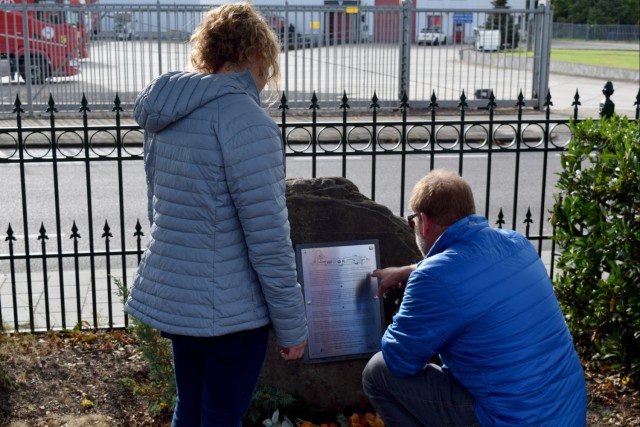 Two people read the text on a memorial plaque.