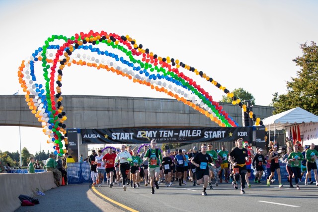Dozens of runners are racing away from the starting line of the Army Ten-Miler race. There are multicolored balloons forming a tall arch over the starting line.