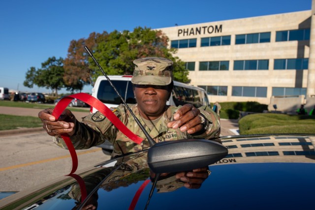Col. Lakicia Stokes, U.S. Army Garrison-Fort Cavazos commander, reaches to tie a red ribbon on the antenna of her car, signifying her support to Tie One On for Safety. (U.S. Army photo by Samantha Harms, Fort Cavazos Public Affairs)