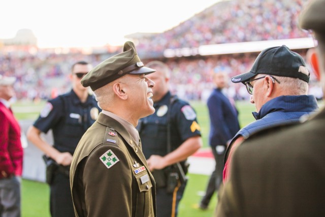 Chief Warrant Officer 5 Mike Corsaro, Chief Warrant Officer, Aviation Branch, shares a laugh with Veterans during the “Walk of Heroes” at the Veterans Memorial Stadium on Nov. 18, 2023.