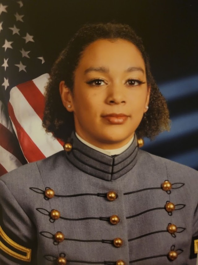 West Point cadet poses in uniform for a headshot in front of the American flag.