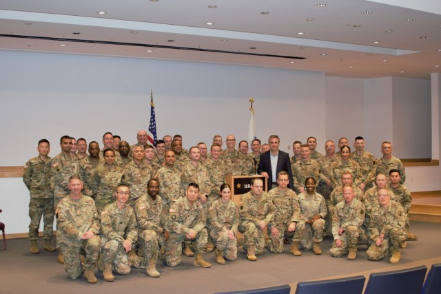 A large group of Soldiers in uniform pose on a stage with a man in a suit.
